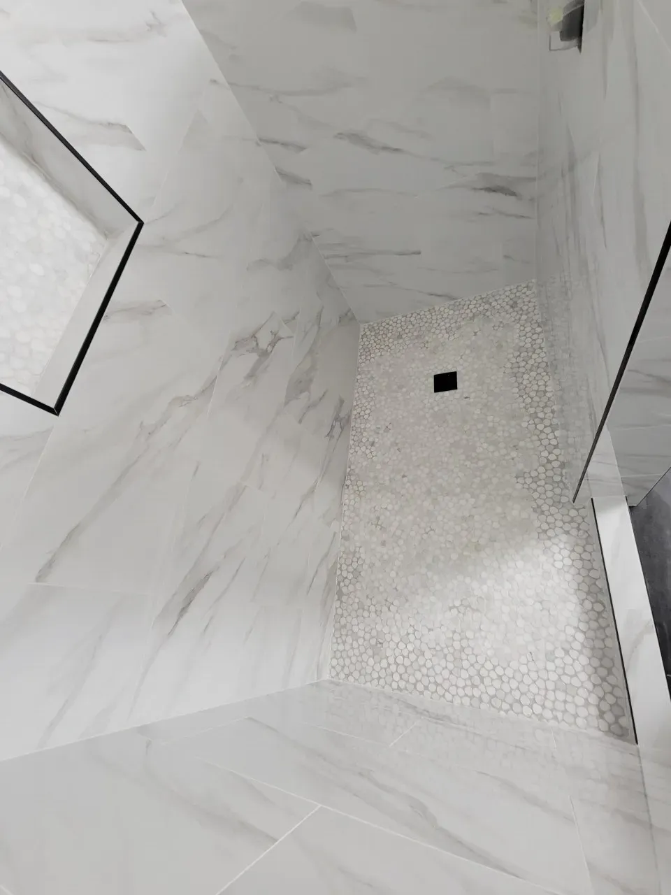 marble-look shower walls with a white pebble floor and glass