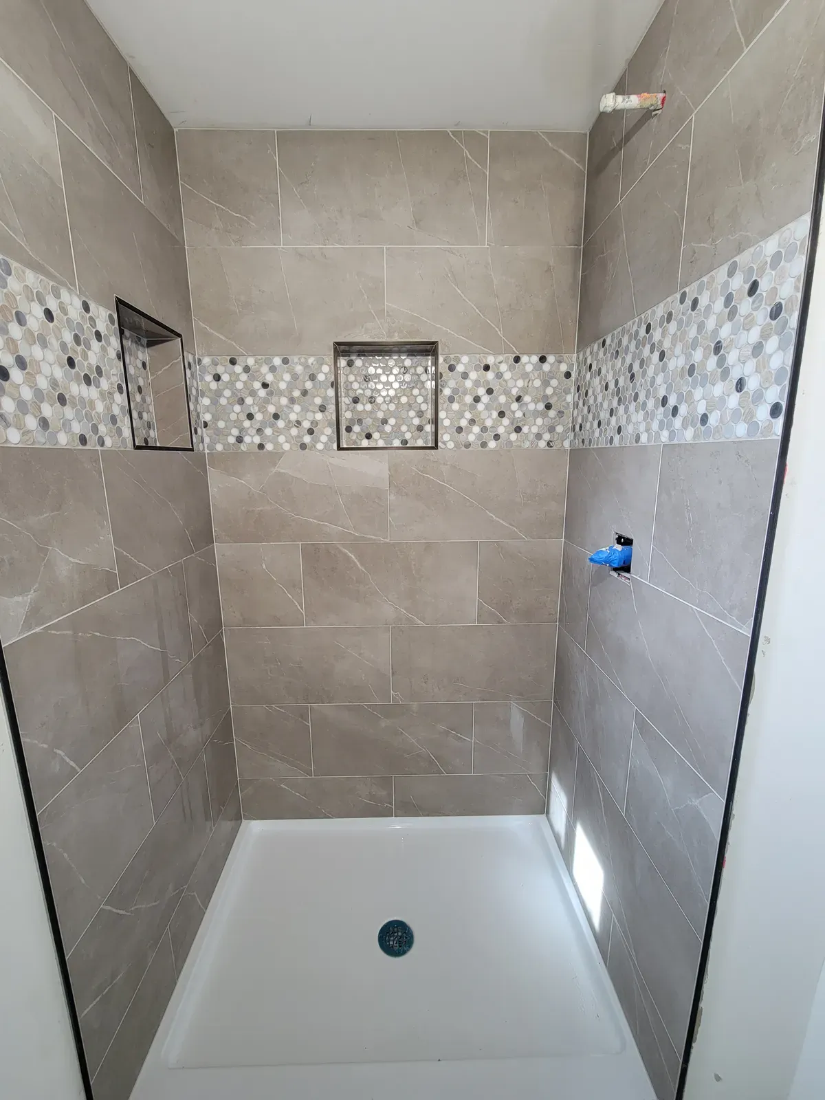 shower with a mosaic accent band and two niches over a solid-surface base, before trim