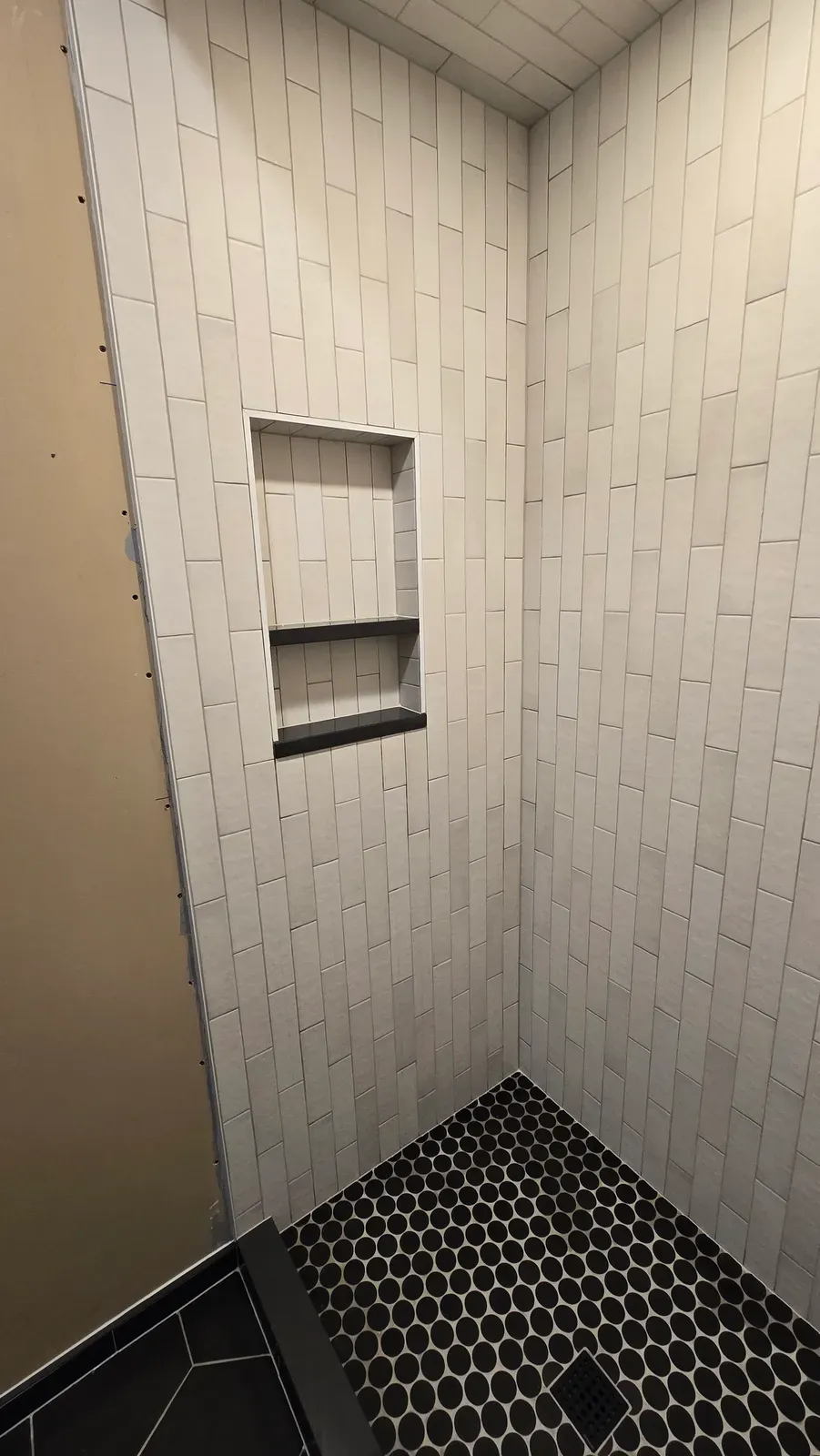 alcove shower in vertical subway tile with a black hex floor and niche